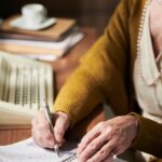 Elderly Hands Writing in Notebook at Desk with Pen
