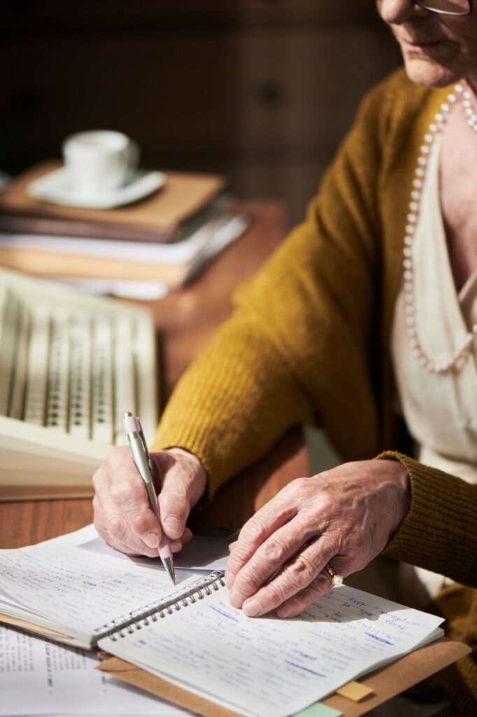 Elderly Hands Writing in Notebook at Desk with Pen