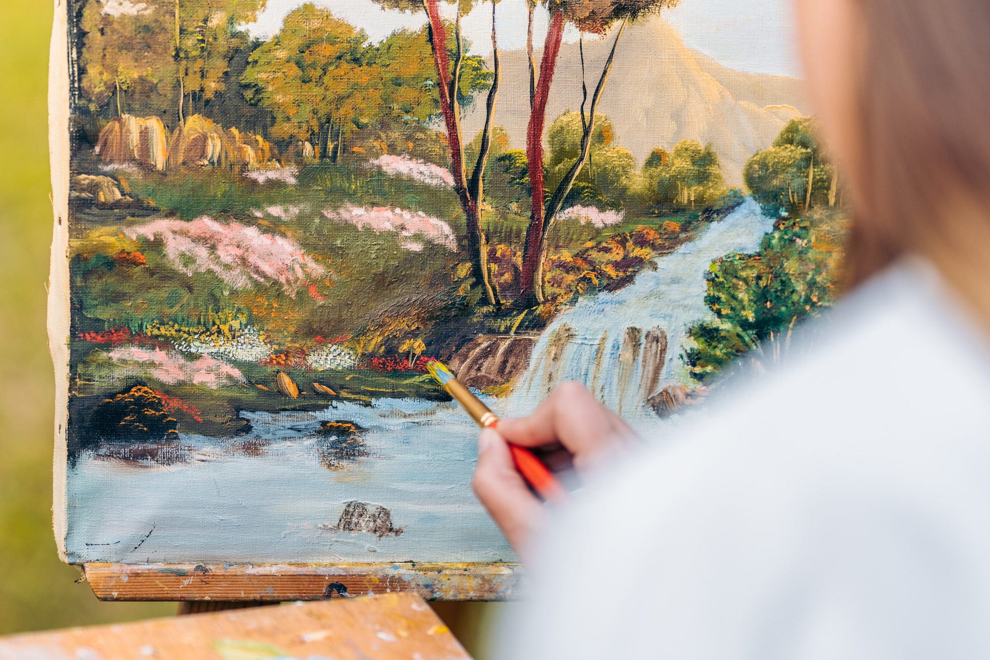 Hand painting with a brush on a canvas with a painting of a forest.